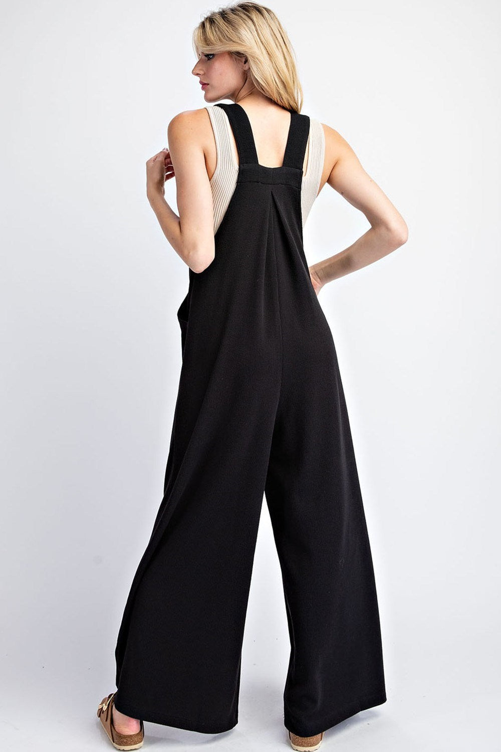 This solid jumpsuit is sleeveless with a square neckline, button adjustable straps, and one front bib pocket. The added pleats provide extra detail, and there are two side hip pockets. It is designed with a wide leg and made of 93% polyester and 7% spandex. This jumpsuit comes in black.