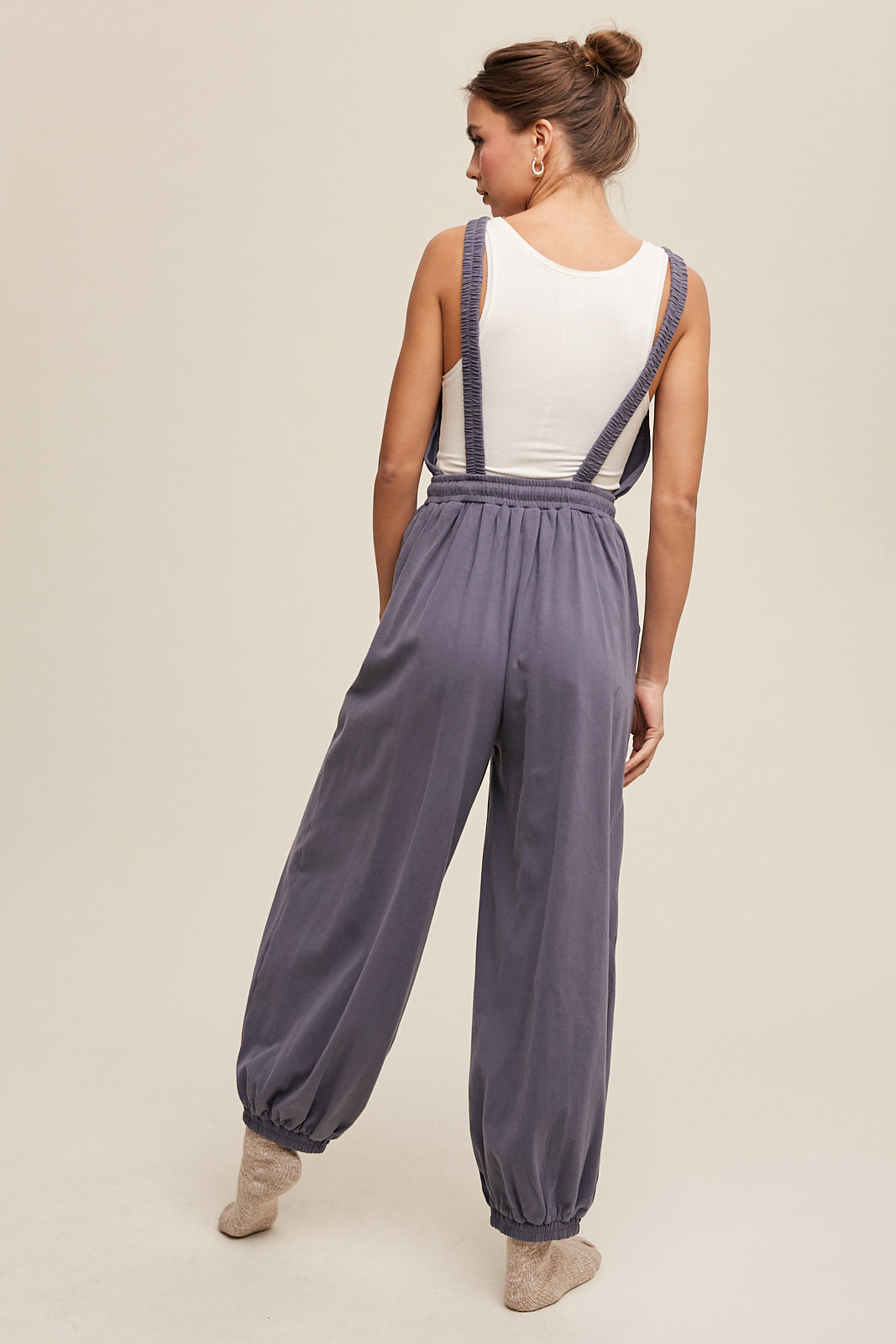 This Tank and Jogger Pants Open Back Knit Jumpsuit features a round neck, elastic shoulder strap, drawstring waist with tie string, and pockets on the pants. Made from 100% cotton in a charcoal color, the jumpsuit is finished with an elastic hem for a comfortable and stylish fit.