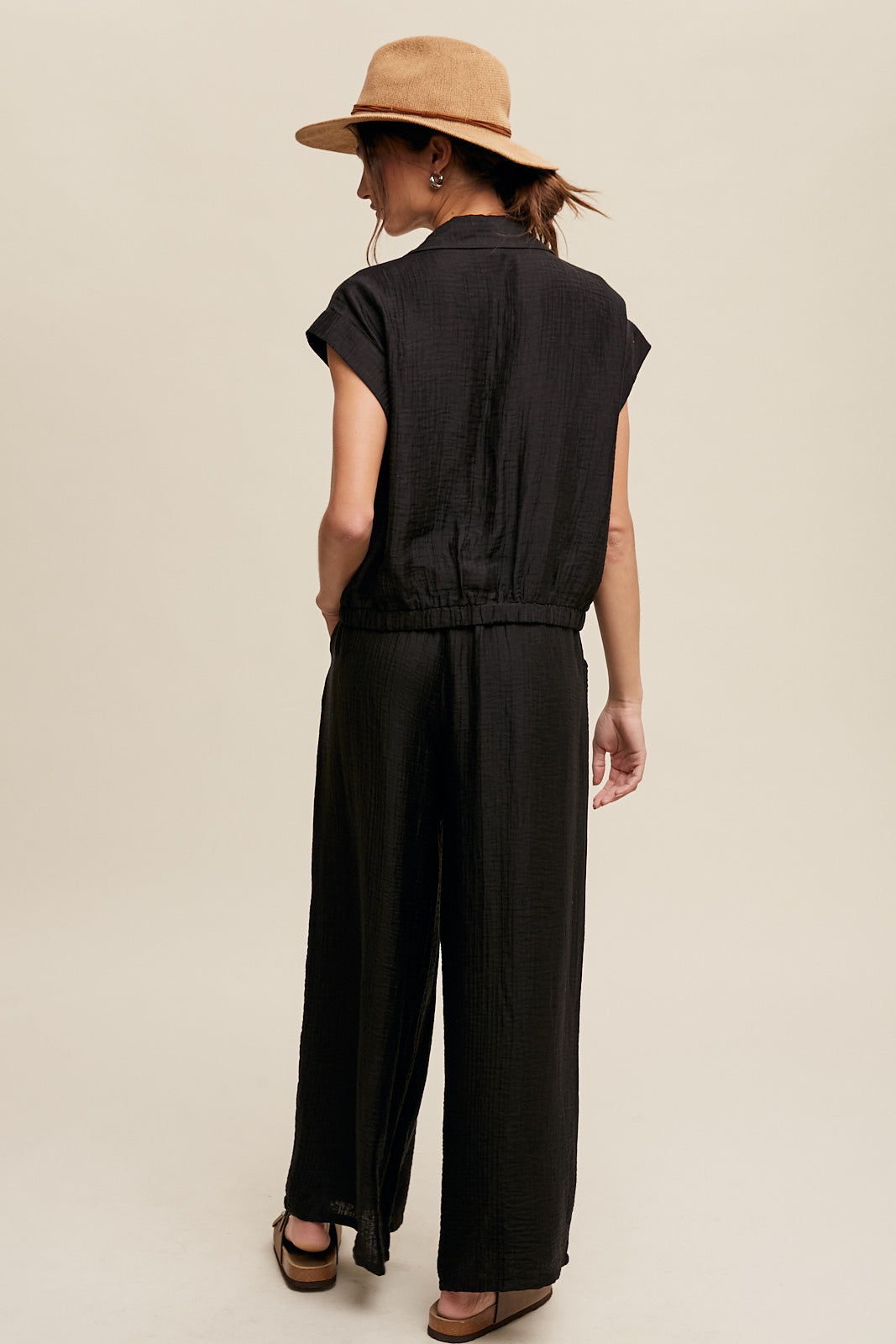 Consisting of a button down top and pleated wide leg pants, this set features a collared neck, short sleeves, and an elastic hem. The pants are designed with wide legs, pockets on the side seam, an elasticized drawstring waist with a tie string, and a clean hem. Made with 45% Rayon, 37% Tencel, and 18% Nylon, this set is available in black.