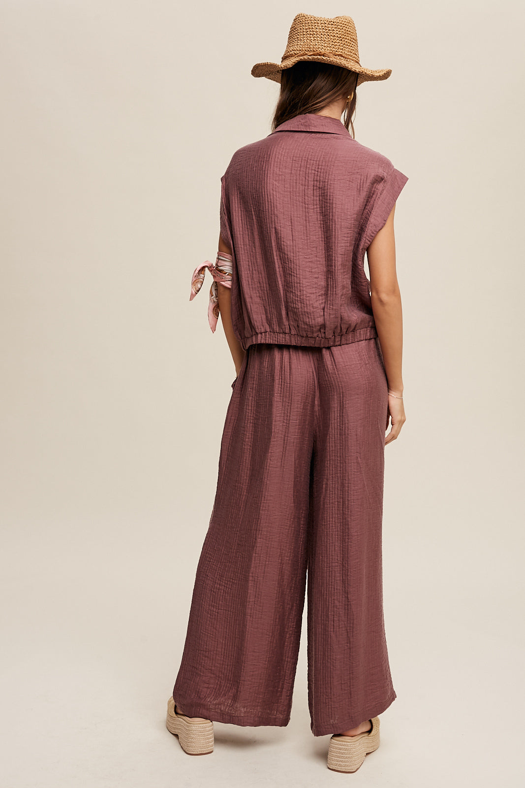 Consisting of a button down top and pleated wide leg pants, this set features a collared neck, short sleeves, and an elastic hem. The pants are designed with wide legs, pockets on the side seam, an elasticized drawstring waist with a tie string, and a clean hem. Made with 45% Rayon, 37% Tencel, and 18% Nylon, this set is available in Red Bean.