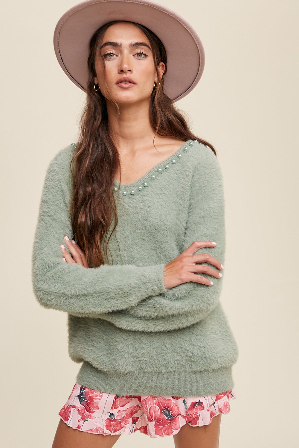 The Deep V-Neck Peal Detail Fuzzy Knit Sweater is composed of a soft touch Fuzzy Knit material, featuring a deep V-neckline and delicate pearl detailing. It boasts long sleeves and is finished with ribbed accents on the neck, cuffs and hem. Made of 65% acrylic and 35% polyester, this sweater is available in Sage.