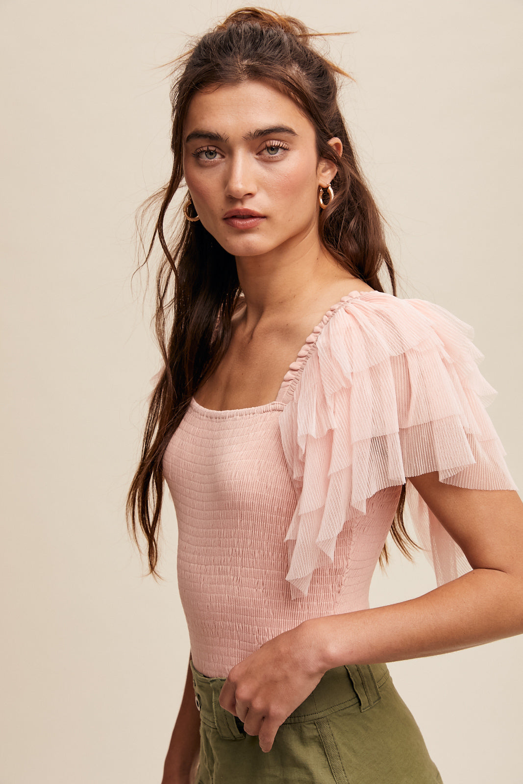 This bodysuit features tiered ruffle sleeves and a square neckline with elastic, creating a layered and smocked design for a chic finish. Available in Light Blush, it is made from 92% Rayon and 8% Spandex for a comfortable fit. The bottom hem is secured with snap-on buttons.