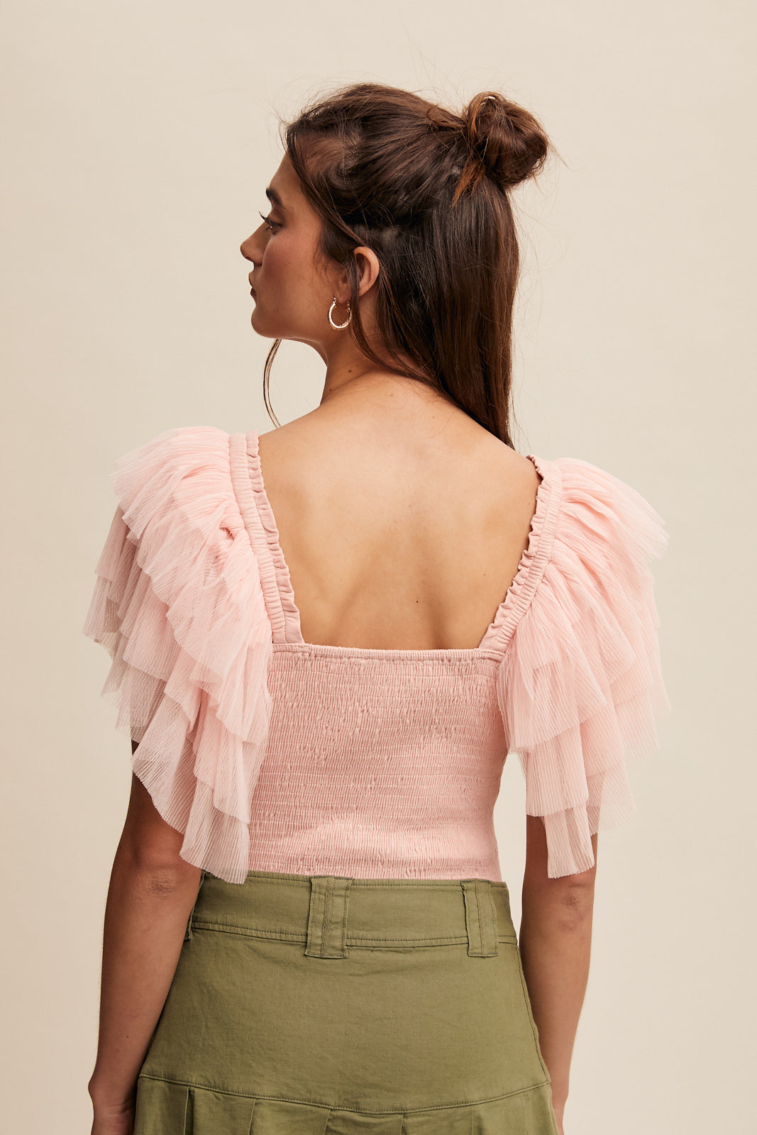 This bodysuit features tiered ruffle sleeves and a square neckline with elastic, creating a layered and smocked design for a chic finish. Available in Light Blush, it is made from 92% Rayon and 8% Spandex for a comfortable fit. The bottom hem is secured with snap-on buttons.