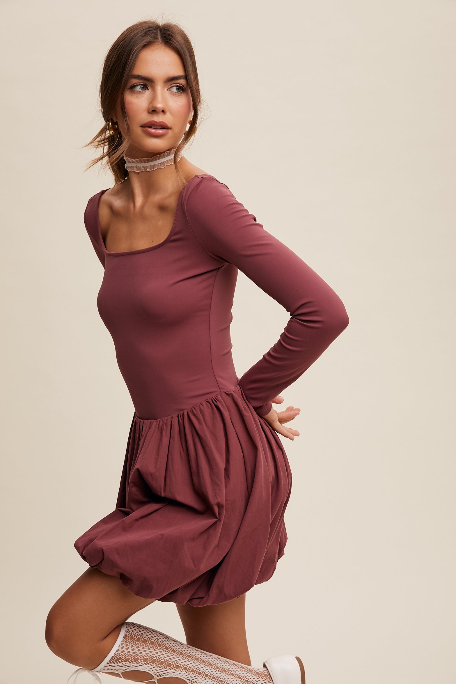 This dress features a square neckline, long sleeves, and a bubble skirt with a built-in romper liner. The top and shorts have a fitted, stretched design, and the skirt is made of cotton with a balloon layer. It comes in the color grape and is composed of 76% nylon and 24% spandex.