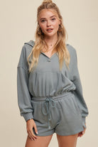 Expertly crafted from 100% cotton, this French terry hoodie romper features a low V neckline and long sleeves with elastic bands on the openings. The adjustable strap with elastic band on the waistband provides a comfortable fit, while the pocket on the side front bottom shorts adds functionality. This piece is completed with a clean hem and is available in a Sage color.