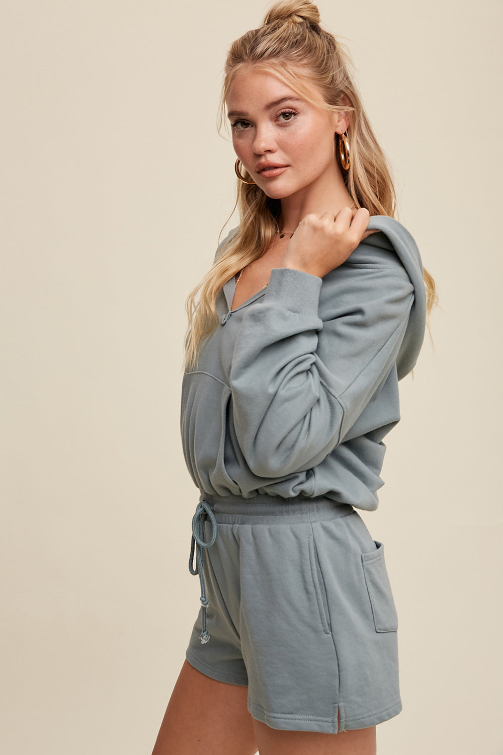 Expertly crafted from 100% cotton, this French terry hoodie romper features a low V neckline and long sleeves with elastic bands on the openings. The adjustable strap with elastic band on the waistband provides a comfortable fit, while the pocket on the side front bottom shorts adds functionality. This piece is completed with a clean hem and is available in a Sage color.