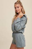 Expertly crafted from 100% cotton, this French terry hoodie romper features a low V neckline and long sleeves with elastic bands on the openings. The adjustable strap with elastic band on the waistband provides a comfortable fit, while the pocket on the side front bottom shorts adds functionality. This piece is completed with a clean hem and is available in a Sage color.