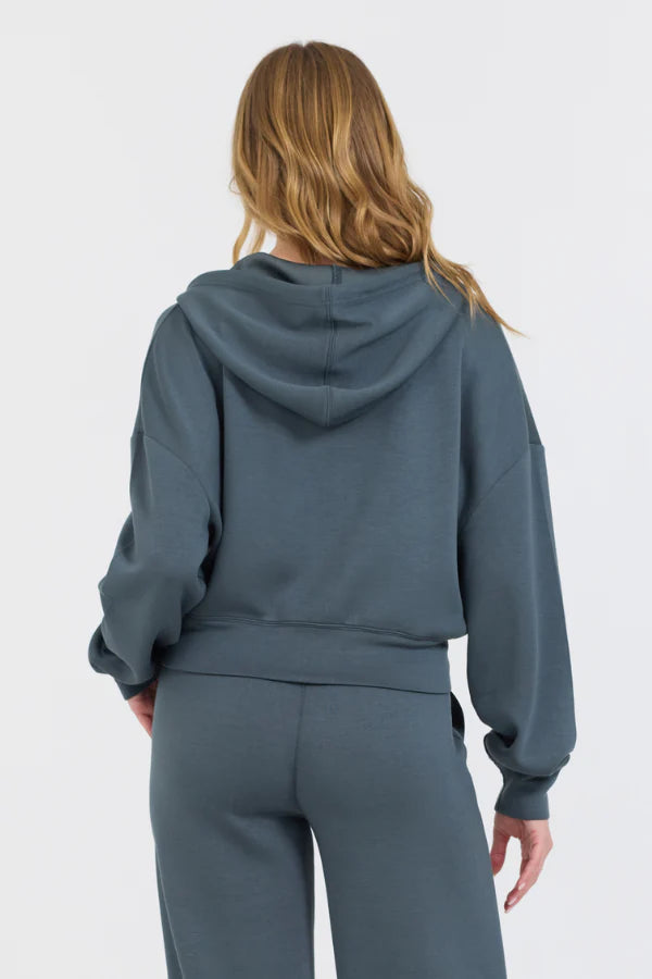 The Mountain Grey Cloud Fleece Crop Zip boasts an adjustable drawstring hood and a zip-up design, crafted from a blend of 49% Modal, 45% Polyester, and 6% Spandex for a comfortable and stylish fit.